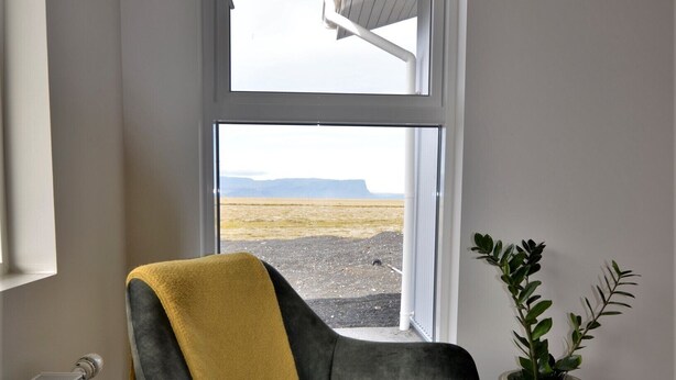 A modern chair with a yellow throw blanket, positioned next to a window with a view of a landscape. - Stracta Apartments (Kirkjubaejarklaustur)