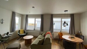 A modern living room with a sofa, chairs, a dining table, and large windows. - Stracta Apartments (Kirkjubaejarklaustur)