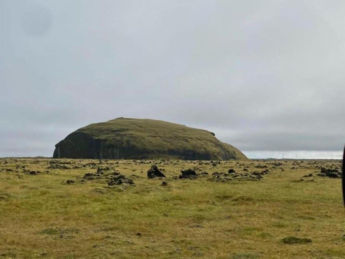 A large, isolated rock formation in a grassy field.
