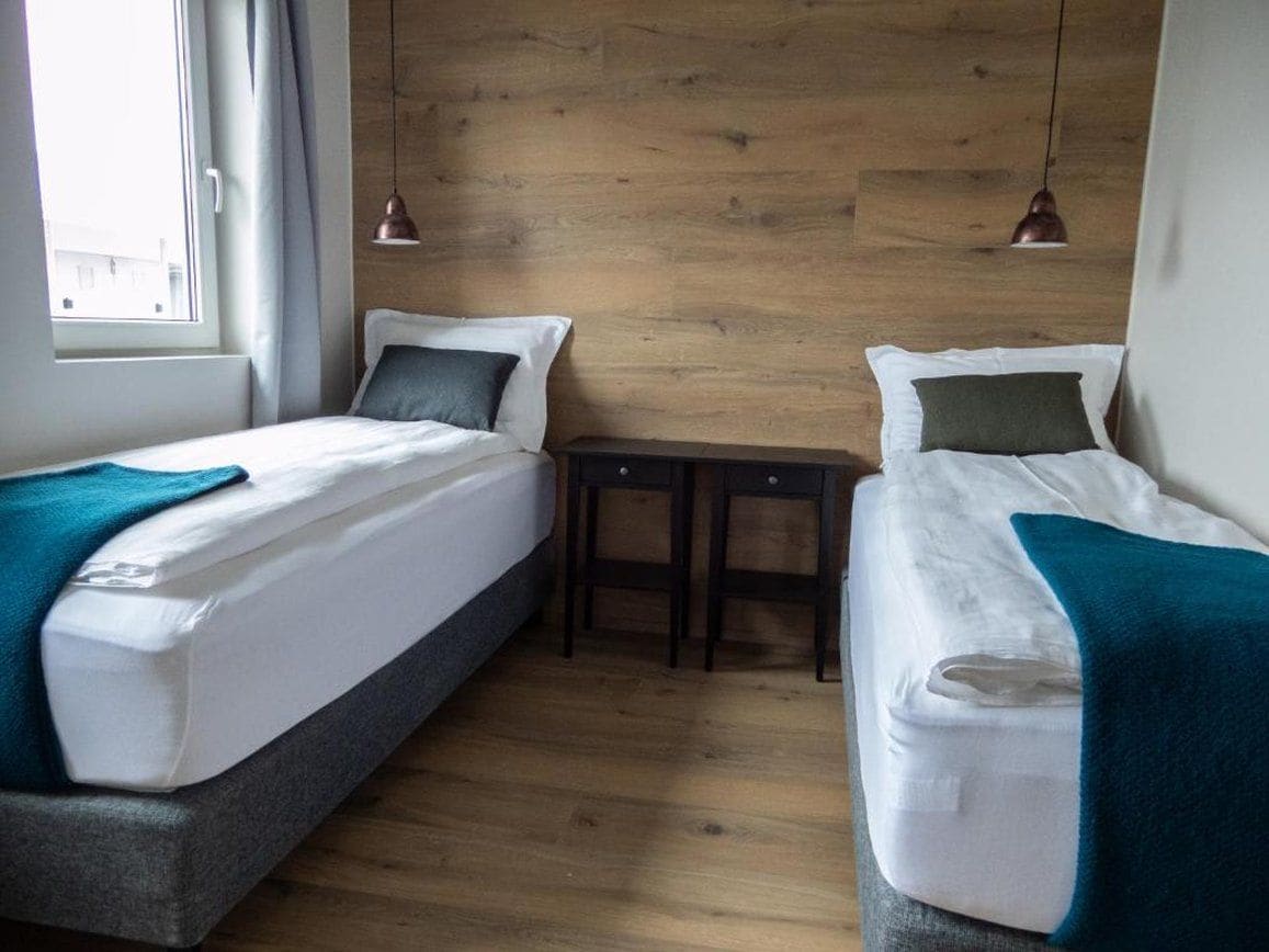 Una habitación con dos camas, una mesita y una ventana.
