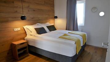 A bedroom with a wooden headboard, a bed with white bedding, two bedside lamps, a bedside table, and a window with curtains.
