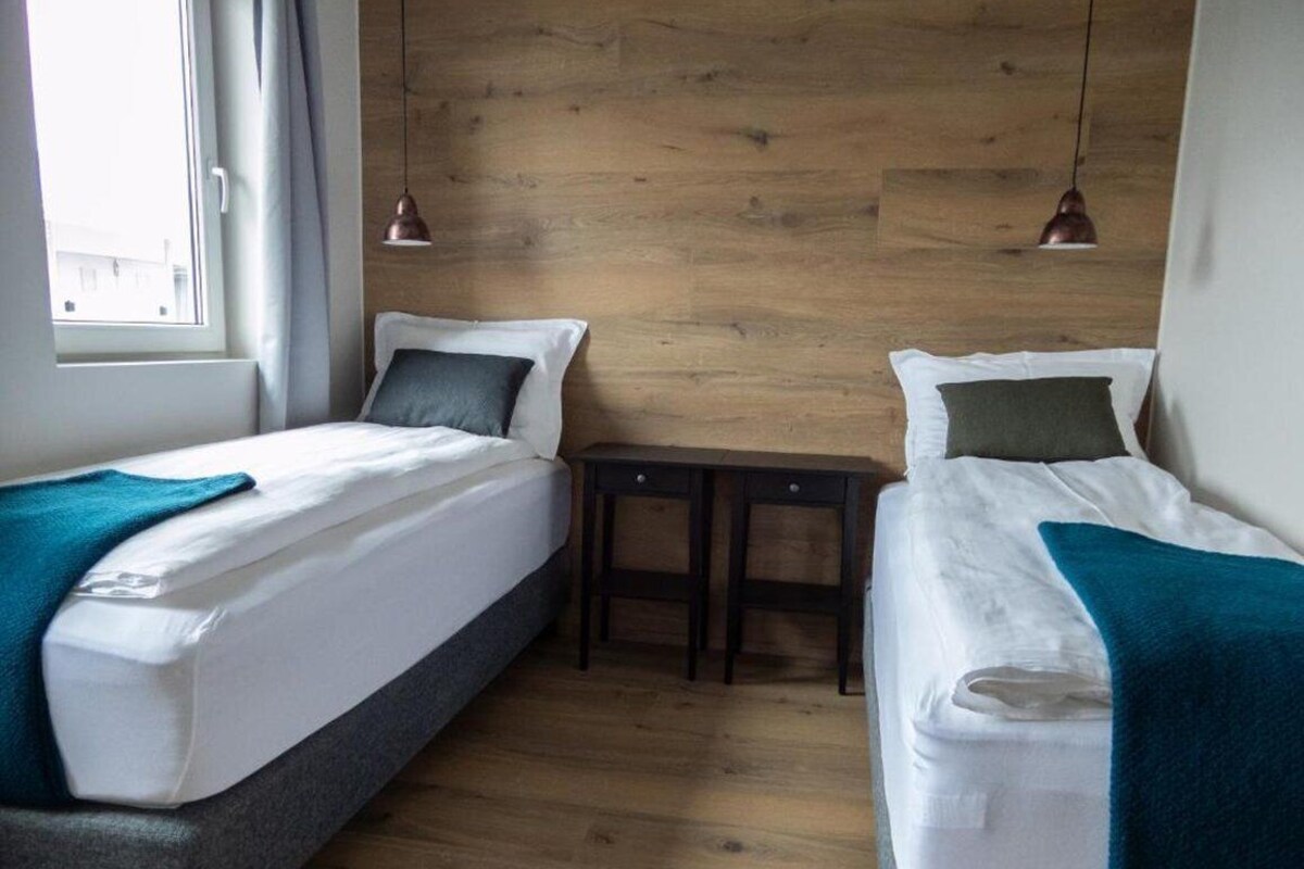Una habitación con dos camas, una mesita y una pared de madera.