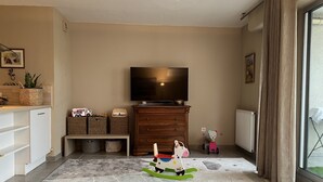 Un salon équipé d’un téléviseur à écran plat, d’un meuble en bois, de paniers en osier et d’un cheval à bascule pour enfant.