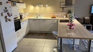 Une cuisine moderne avec des meubles blancs, un four encastré, un évier et un coin repas comprenant une table en bois et des tabourets de bar.