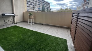 Un balcon avec un petit espace recouvert de gazon synthétique, une imprimante et une plante en pot.