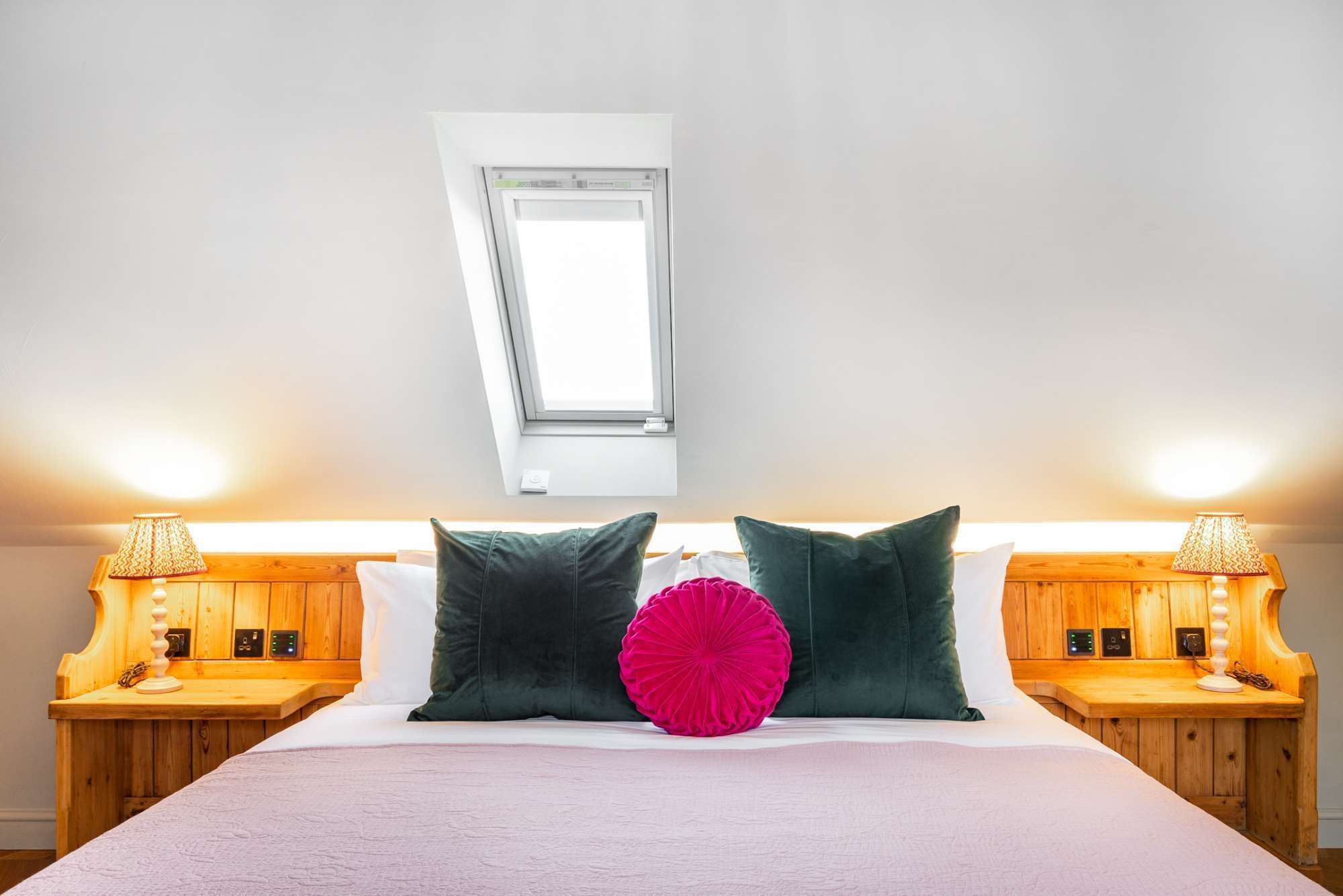 A bedroom with a large bed, two bedside tables with lamps, a skylight, and a wooden headboard.