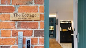 Un muro de ladrillo con un letrero de madera que dice "The Cottage espaisroca.com" y un timbre con teclado.