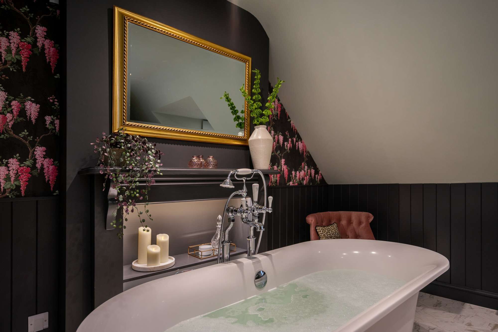 A bathroom with a freestanding bathtub, a mirror with a gold frame, and a wall-mounted shelf with decorative items.