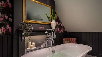 A bathroom with a freestanding bathtub, a mirror with a gold frame, and a wall-mounted shelf with decorative items.