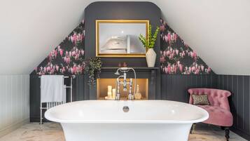 Une salle de bain avec une baignoire sur pieds, un meuble-lavabo avec un miroir et une chaise rose.