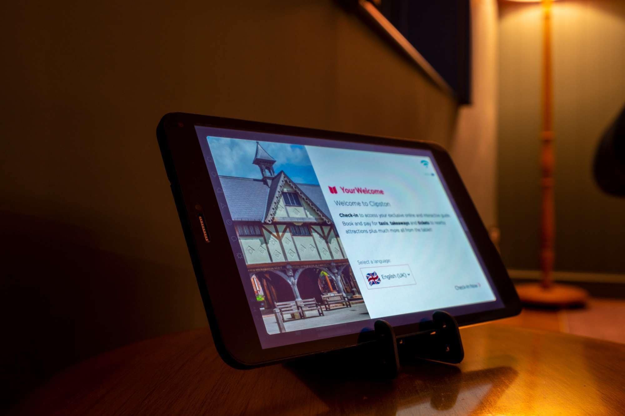 Ein Tablet zeigt eine Begrüßungsseite mit einem Bild eines traditionellen Gebäudes und Informationen zur Buchung und Sprachauswahl.