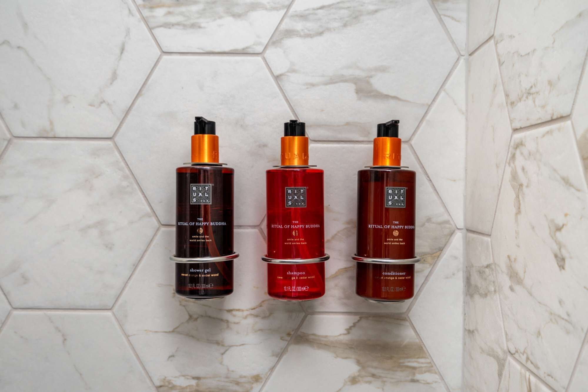 Tres botellas de productos Ritual de Happy Buddha sobre un piso de baldosas.