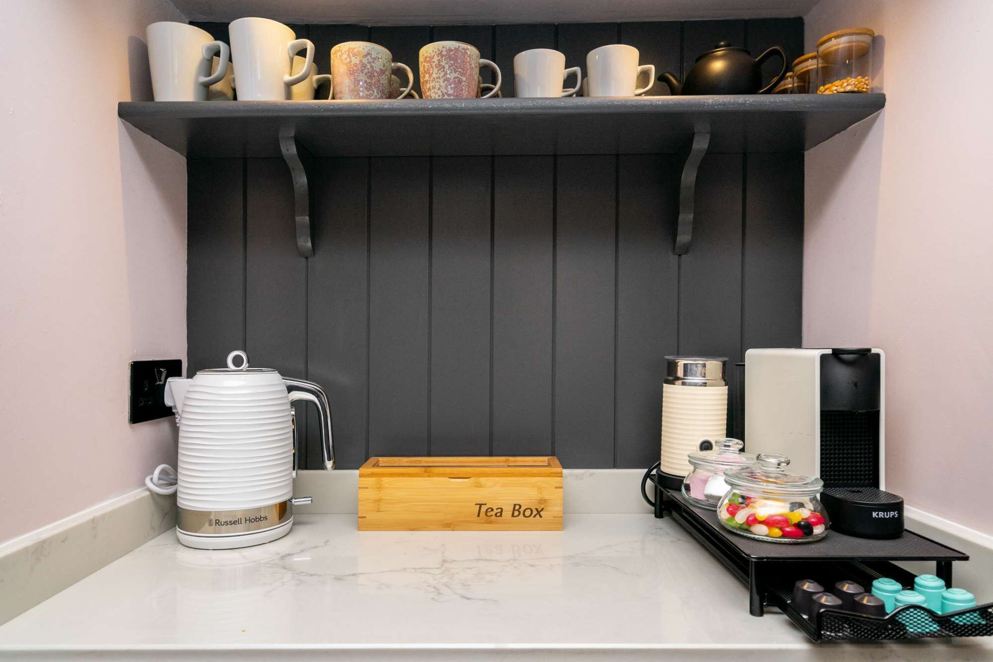 Una zona de cocina con estación de té, que incluye un hervidor, una caja de té y varias tazas y recipientes.