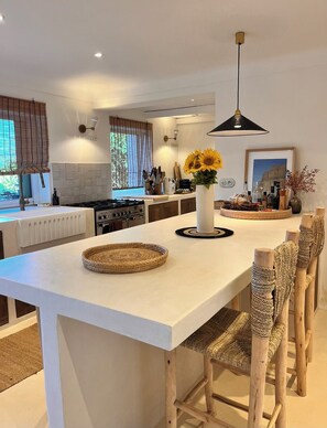 A modern kitchen with a central island, white cabinetry, and a dining area with wooden chairs.