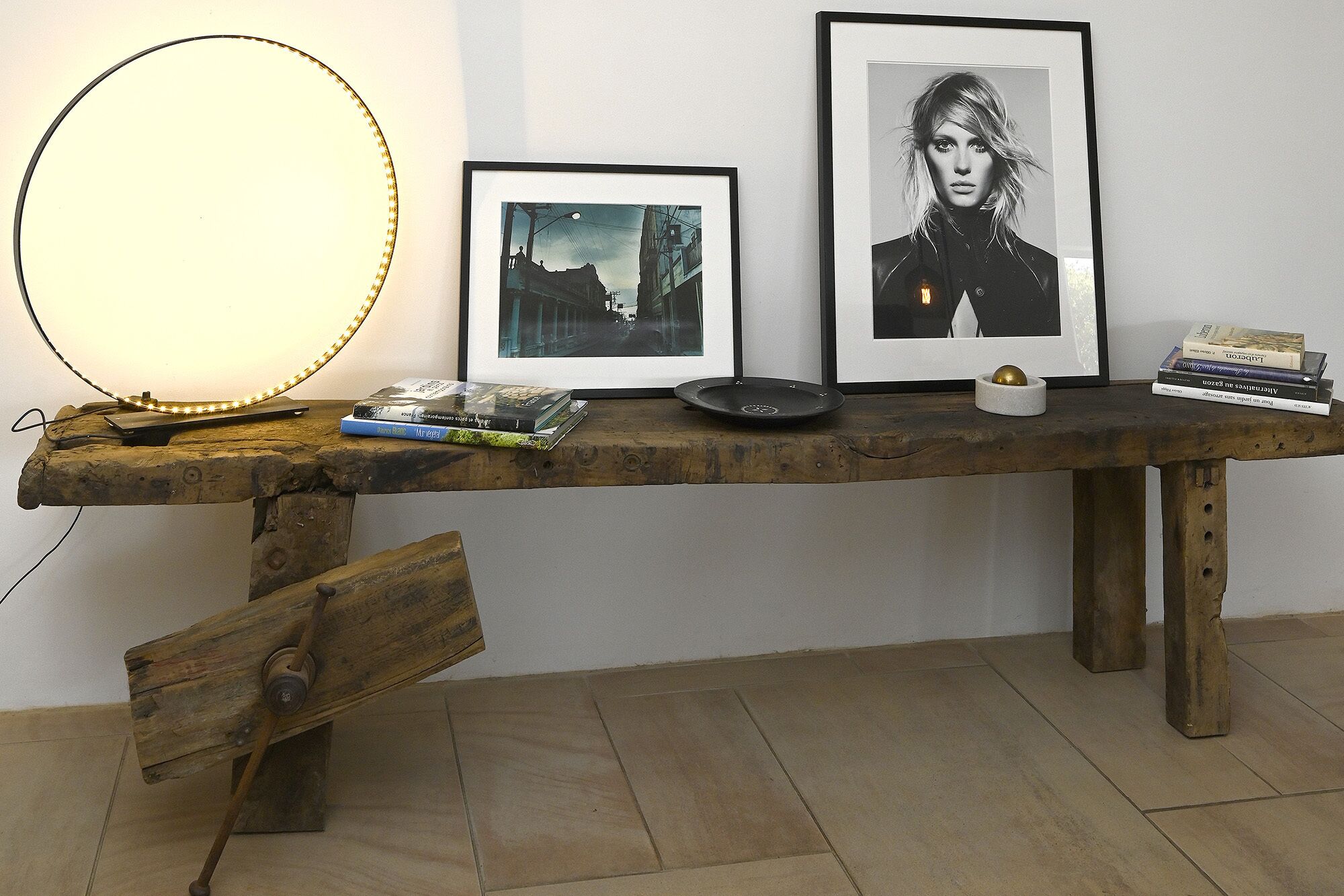 A rustic wooden table with a round light fixture, a framed photograph, a black and white portrait, and some books.