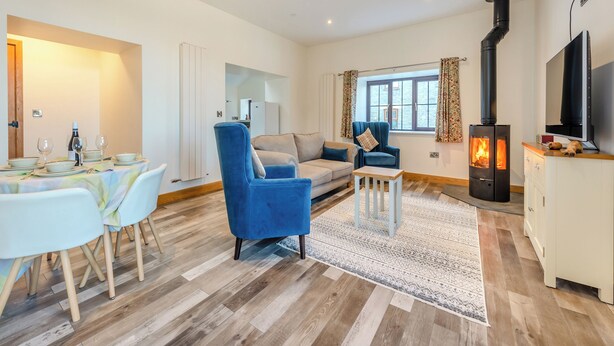 A living room with a sofa, armchair, TV, fireplace, dining area, and a view of the outside. - 2 bedroom accommodation in Lampeter (Lampeter)