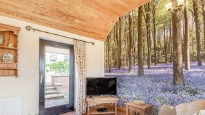 Ein gemütliches Wohnzimmer mit großem Fernseher, Holzmöbeln und einer Wandmalerei von einem Wald.