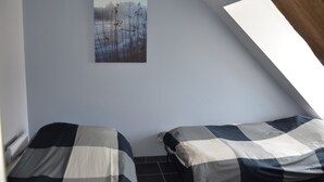 Une chambre de dortoir avec deux lits, un tableau accroché au mur et un plafond en pente.