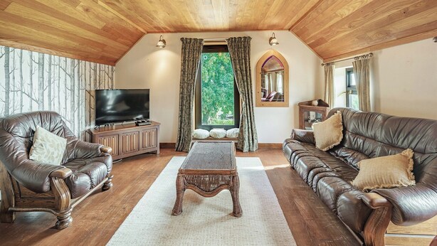 Un salon chaleureux avec un plafond et des murs en bois, un téléviseur, deux canapés en cuir, une table basse en osier et une fenêtre avec des rideaux.