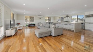 Amplia sala de estar con sofá seccional gris, piso de madera y cocina con isla central y taburetes de bar.