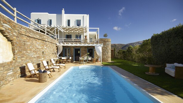 Un espace aménagé au bord de la piscine, avec des chaises longues, un mur en pierre et un bâtiment blanc agrémenté de touches de bleu.