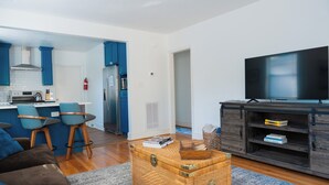 A modern living room with a sofa, a coffee table, a TV, and a kitchen area with blue cabinets and a refrigerator. - Rest Easy : King Bed : Downtown & Ft. Jackson 2Bd 1Bth (Columbia)