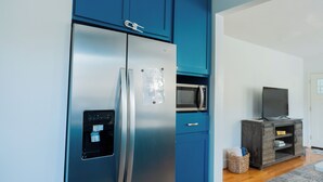 A modern kitchen with a stainless steel refrigerator, a microwave, and a dark wooden cabinet with a television on top. - Rest Easy : King Bed : Downtown & Ft. Jackson 2Bd 1Bth (Columbia)