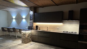 A modern kitchen with a stone accent wall, a built-in gas stove, and a bar area with stools. - Villa Corleone  (Piemonte)