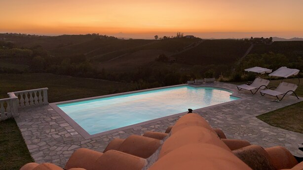 A swimming pool with lounge chairs and a stone pathway, surrounded by hills and a sunset view. - Villa Corleone  (Piemonte)