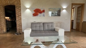 A living room with a grey sofa, a glass coffee table, and two wall-mounted lights. - Villa Corleone  (Piemonte)