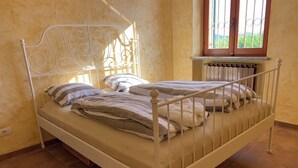 A white metal bed with a decorative headboard in a room with beige walls and a window with bars. - Villa Corleone  (Piemonte)