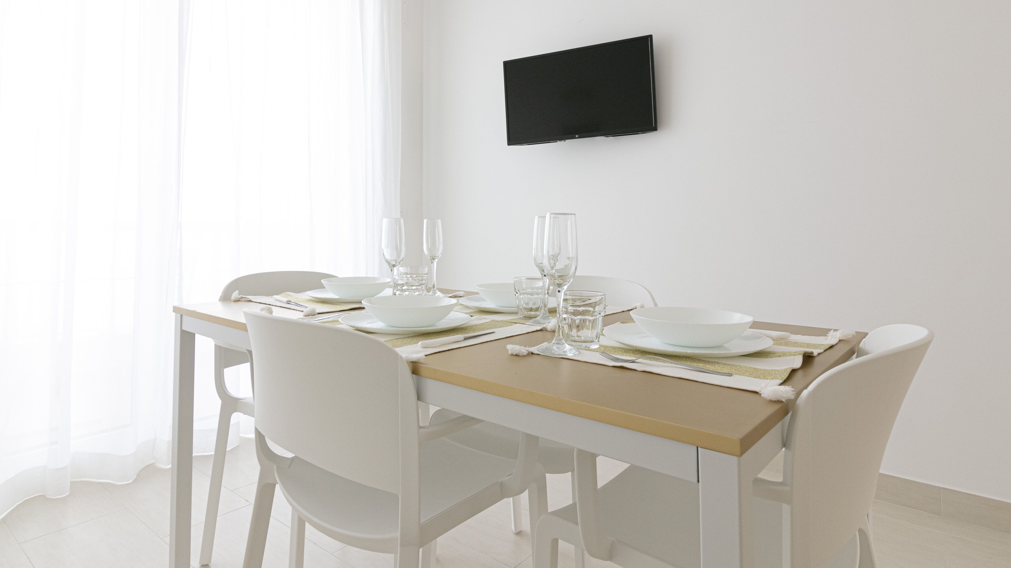 A dining table set with white chairs, plates, glasses, and cutlery.