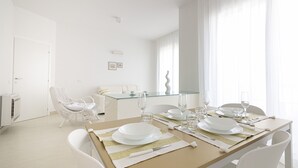 A dining area with a table set for four, a white chair, and a glass-top dining table. - Rivazzurra Homes - 28 (Termoli)