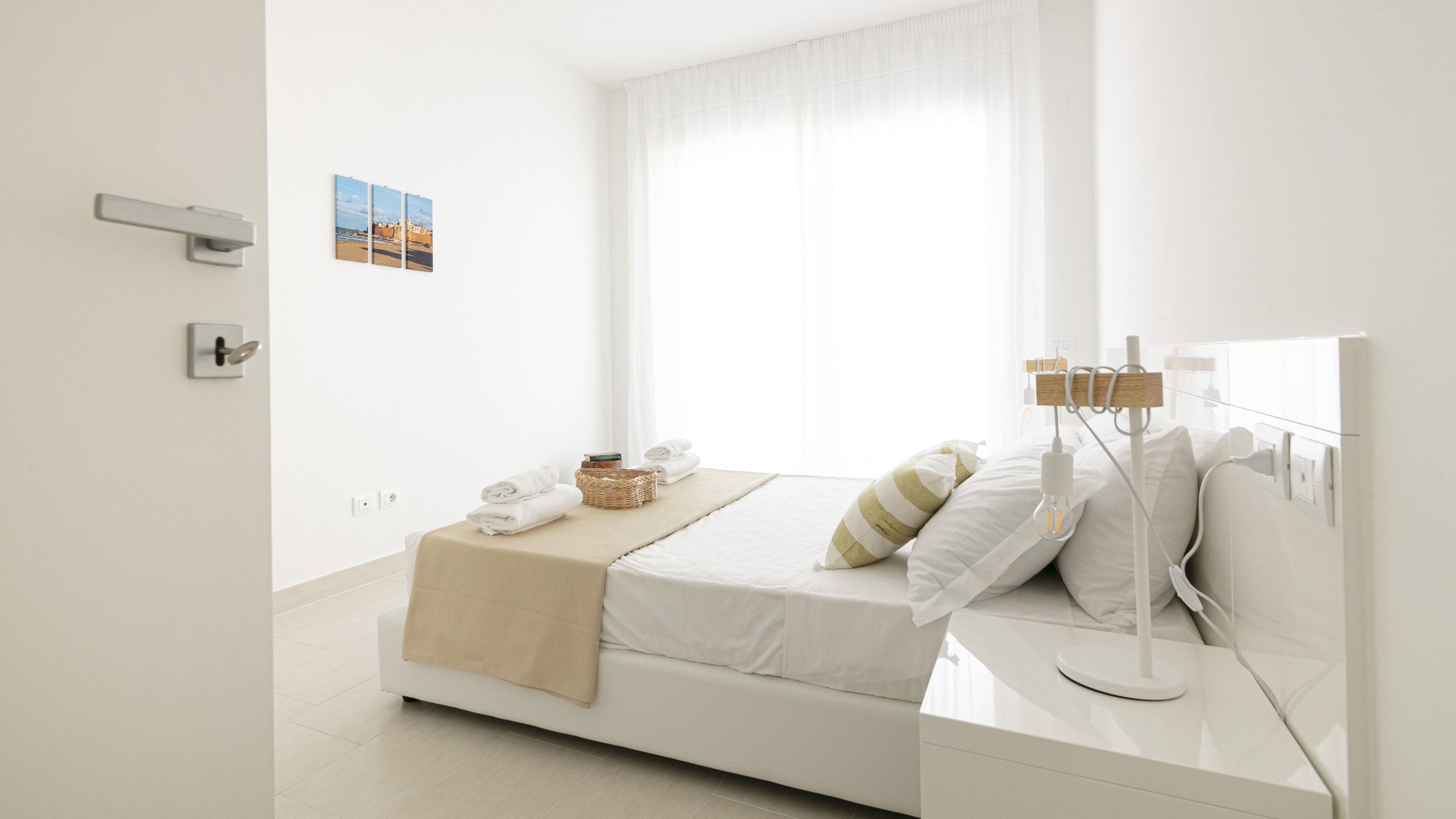 A minimalist bedroom with a bed, bedside table, and a window with sheer curtains.