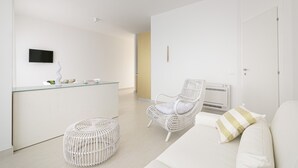 A modern, minimalist living space with a white sofa, a wicker chair, a glass-top coffee table, and a small round ottoman. - Rivazzurra Homes - 28 (Termoli)