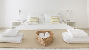 A neatly made bed with white linens and striped pillows, a bedside table with a lamp, and a wicker basket with folded towels on a beige rug. - Rivazzurra Homes - 28 (Termoli)