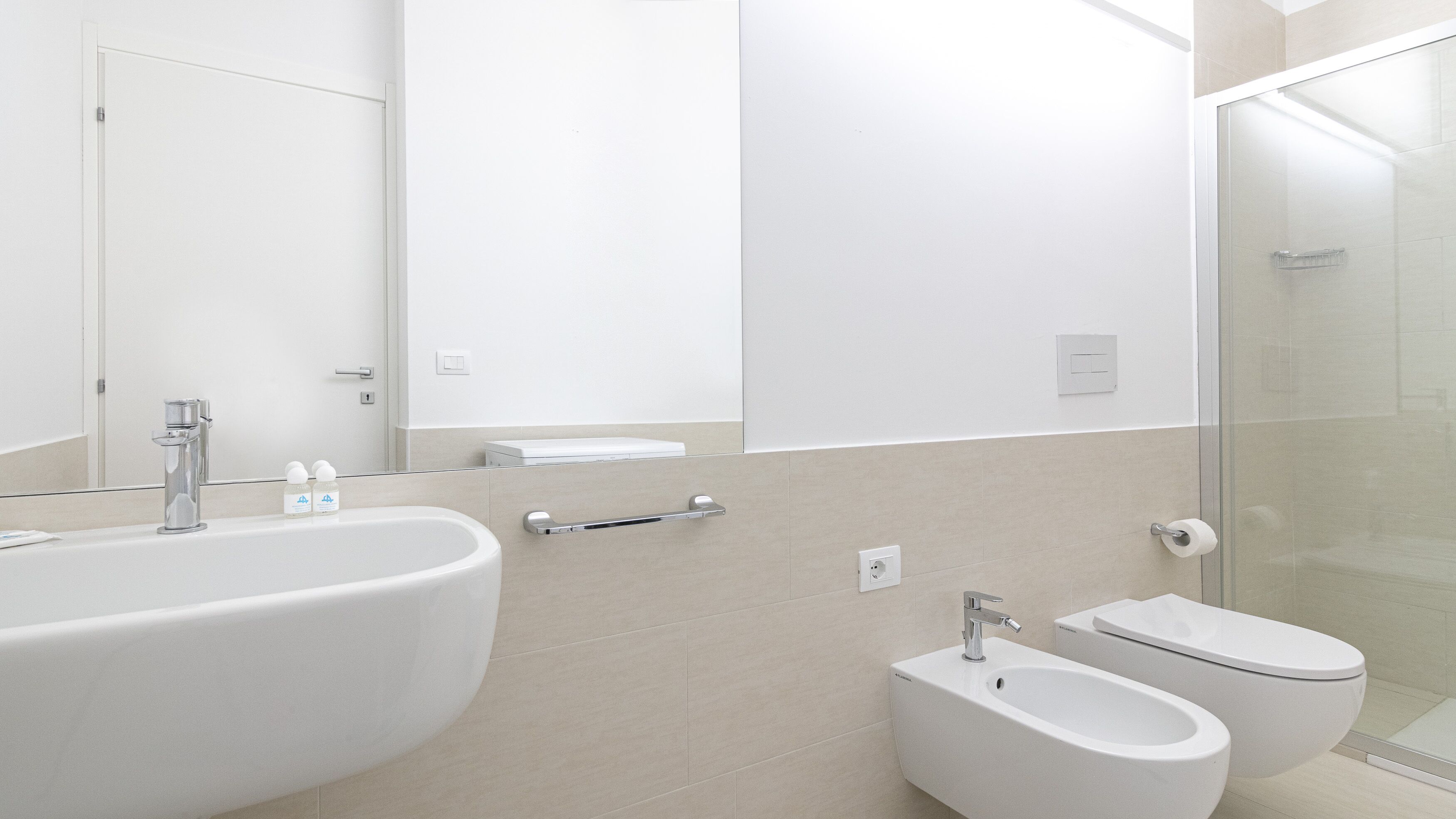 A modern bathroom with a large sink, a bidet, a toilet, and a glass shower enclosure.