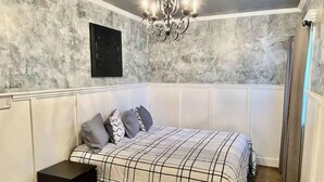 Quarto com cama, penteadeira, mesa de cabeceira, lustre e um quadro na parede.