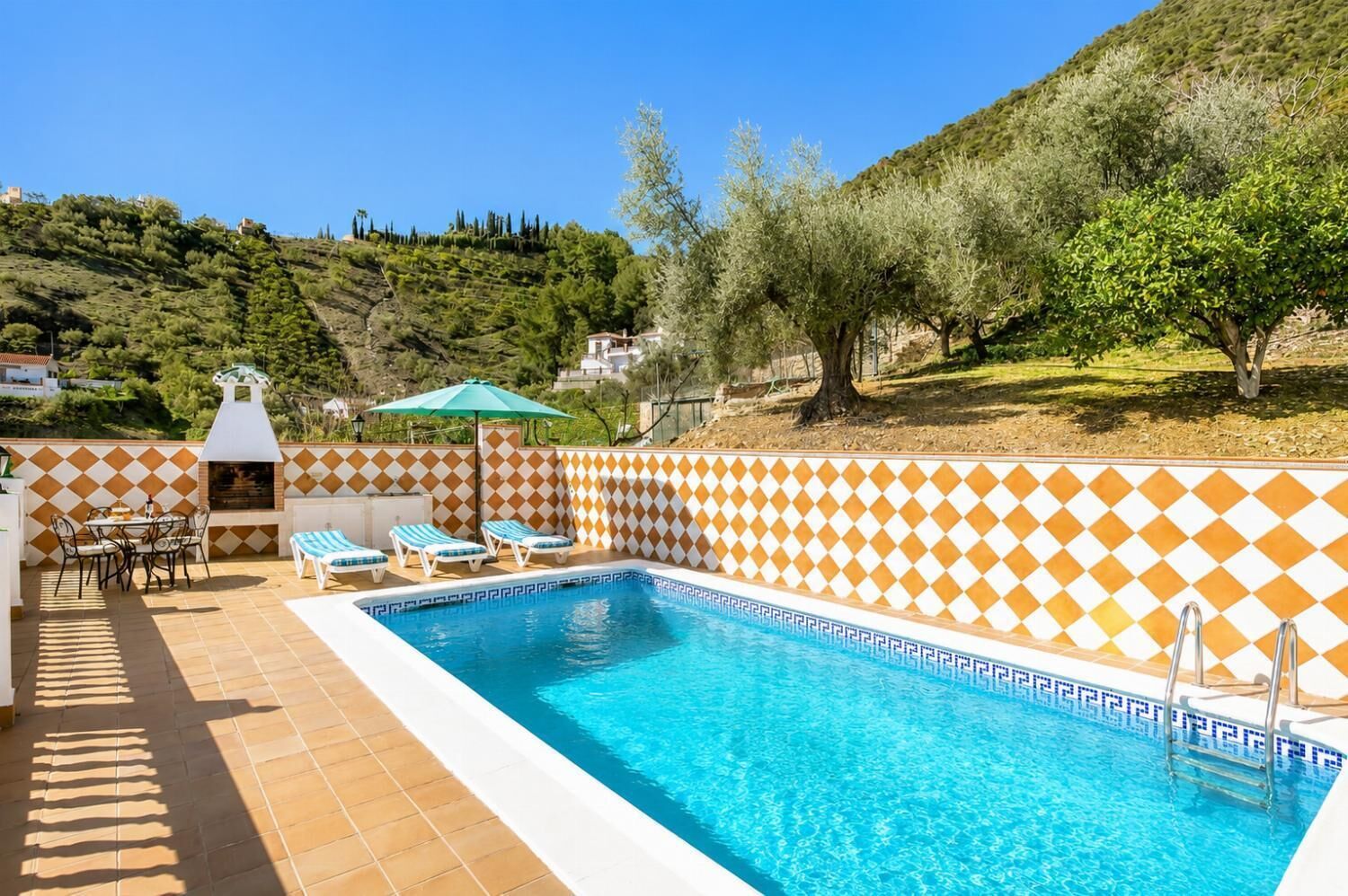 A swimming pool with a checkered tile border, a barbecue area, and lounge chairs.