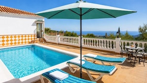 Une piscine avec des chaises longues et un parasol, une vue sur la mer et une terrasse carrelée.