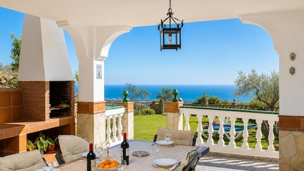 Un espace de restauration en plein air avec vue sur la mer, un four en briques et une table dressée pour deux personnes.