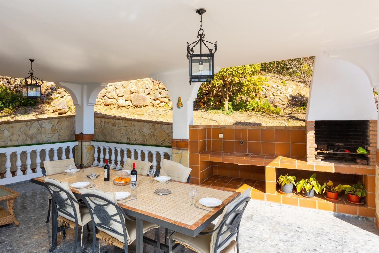An outdoor patio with a stone wall, a wooden table set for dining, and a brick oven.