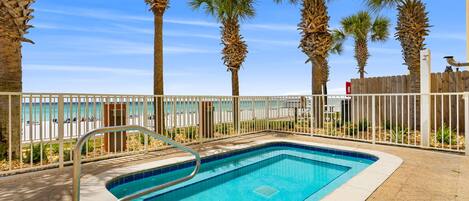 A rectangular pool with a metal ladder, surrounded by a white fence, palm trees, and a view of a beach.