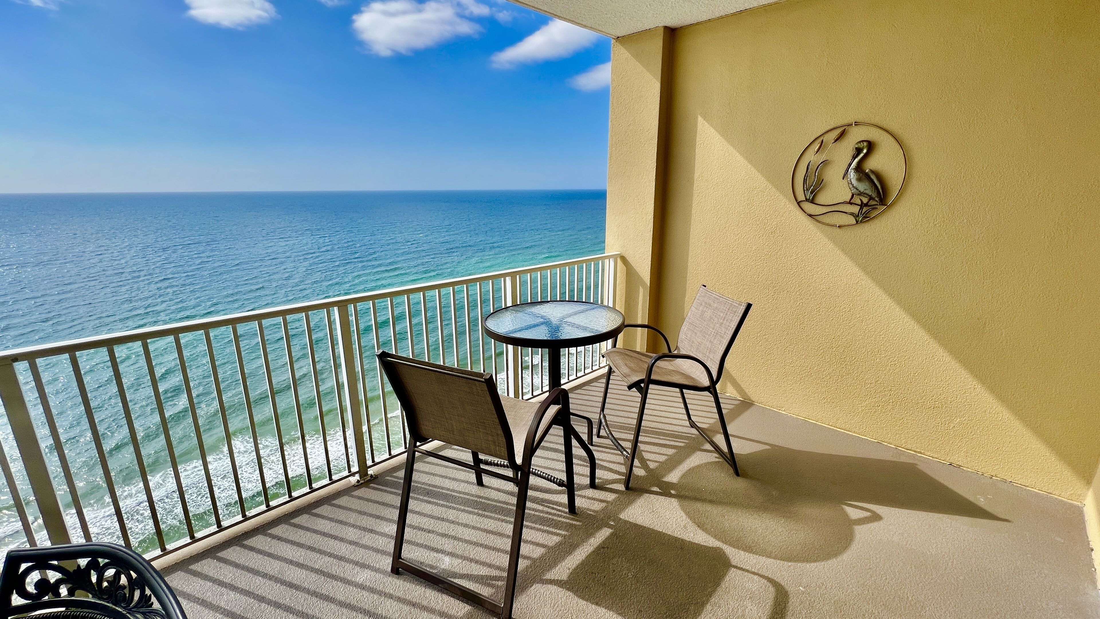 A balcony with a view of the ocean, two chairs, a small table, and a decorative wall piece.
