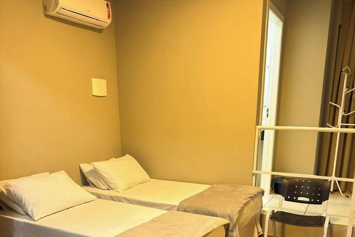 A room with two single beds, a chair, and an air conditioning unit on the wall.
