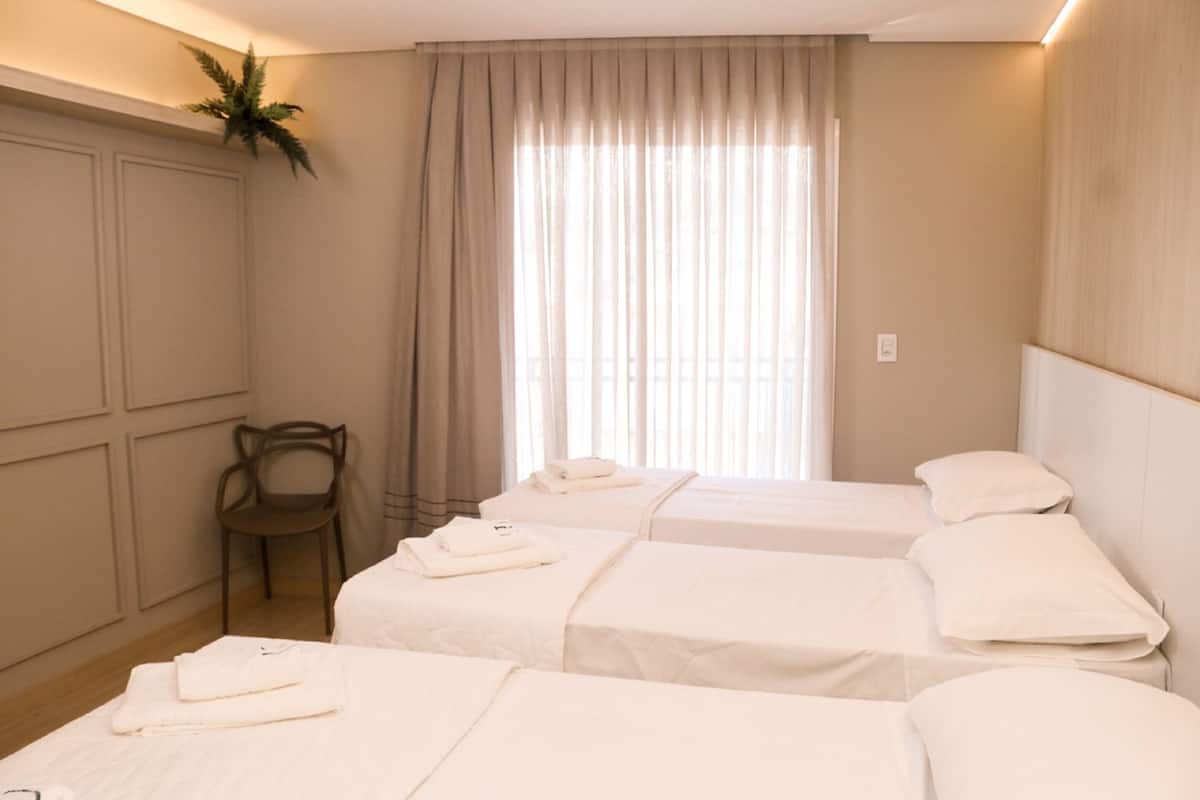 A hotel room with three beds, a chair, and a large window with curtains.