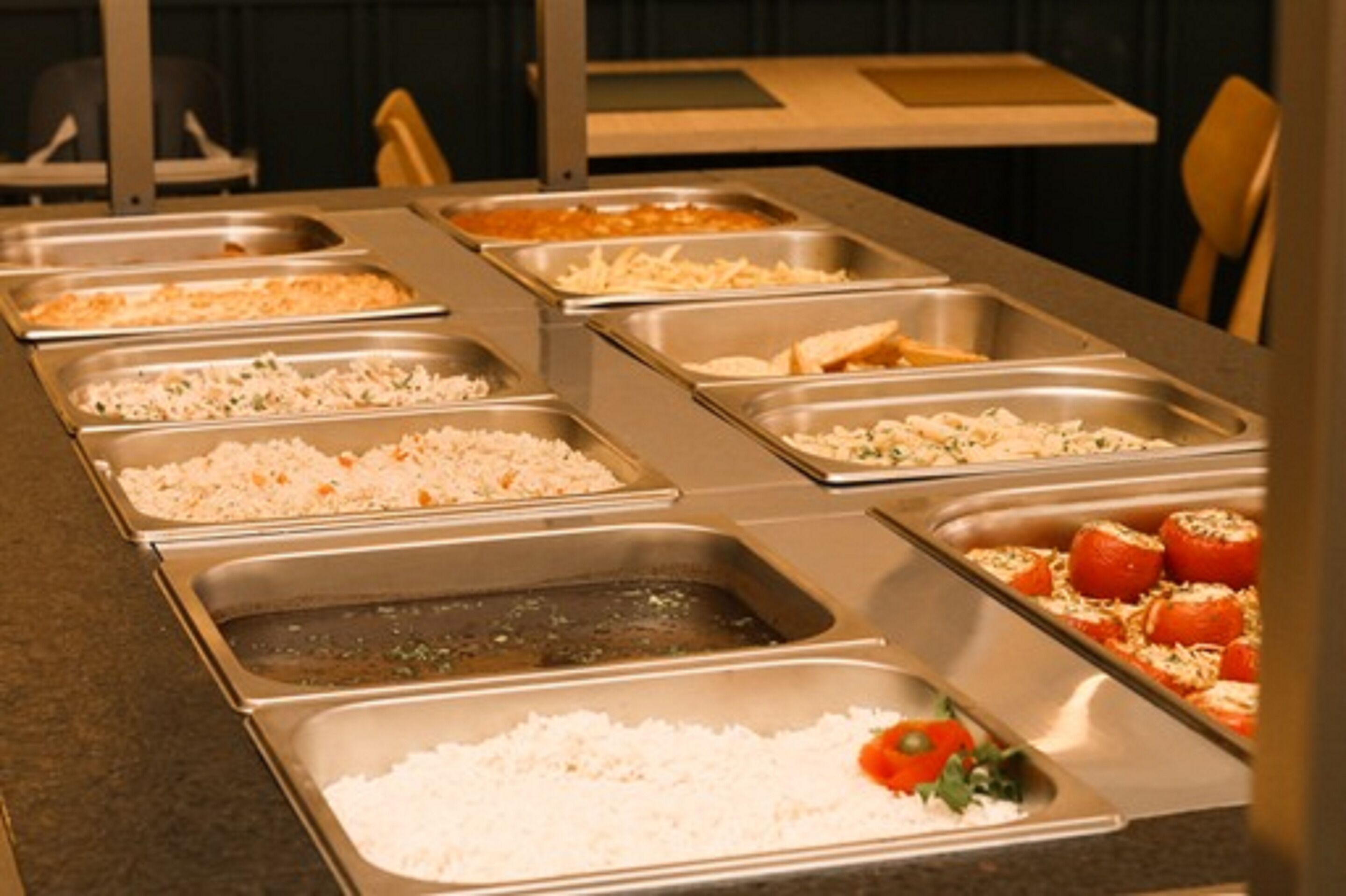 A buffet line with various food options including rice, salads, and stuffed tomatoes.
