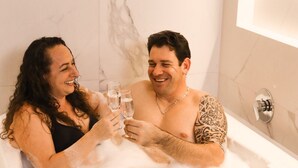 A couple in a bathtub with a marble wall and a modern light fixture. - Estação Termas Hotel (Piratuba)