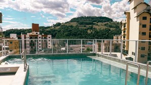 A swimming pool with a glass barrier, surrounded by buildings and a hilly landscape. - Estação Termas Hotel (Piratuba)