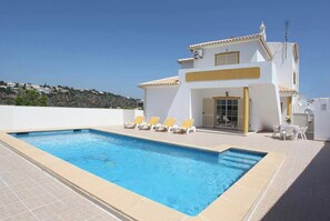 A swimming pool with lounge chairs, a white building with yellow trim, and a clear sky.